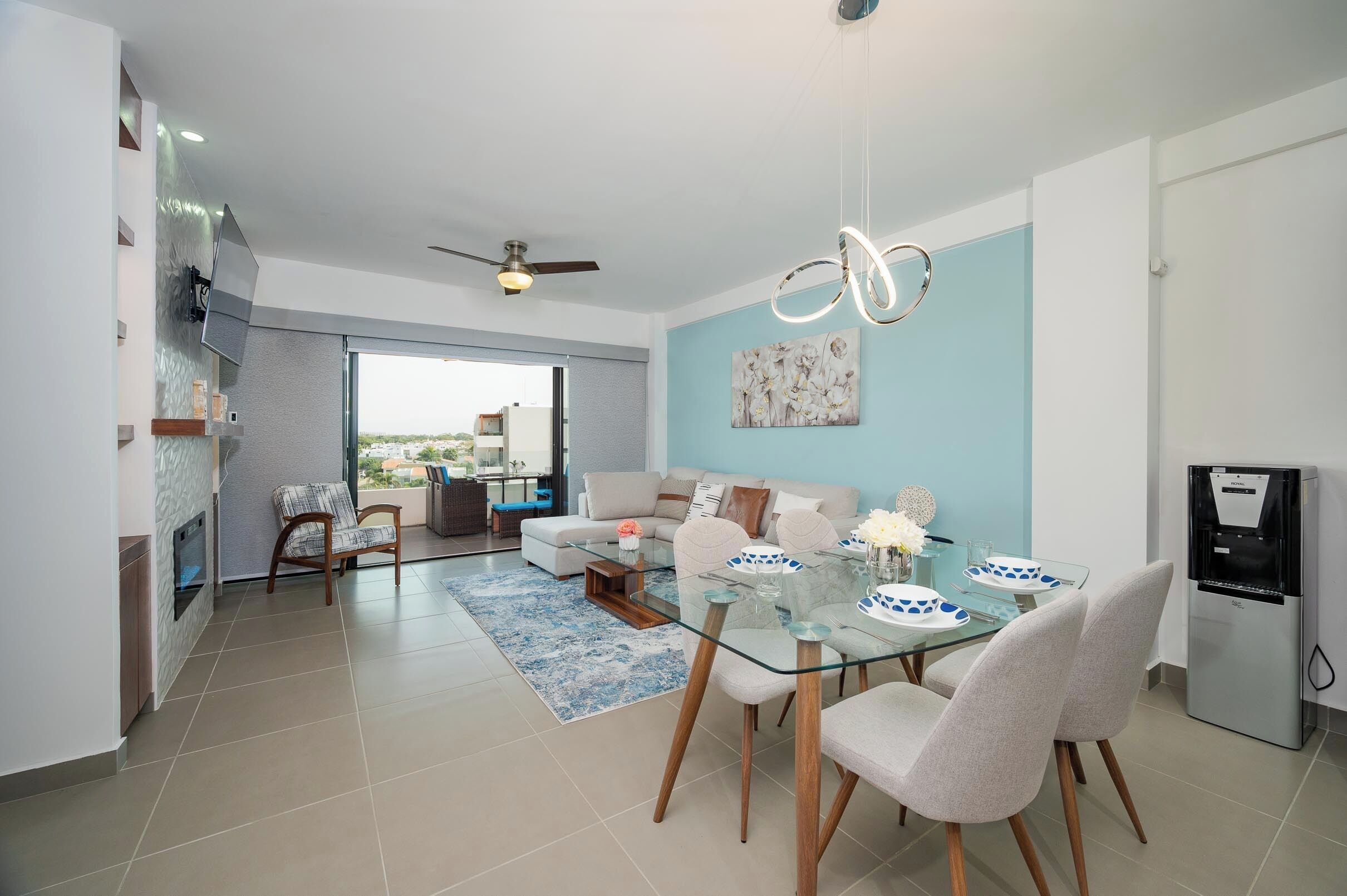 A modern living room with a glass dining table, white sofas, and a blue accent wall.