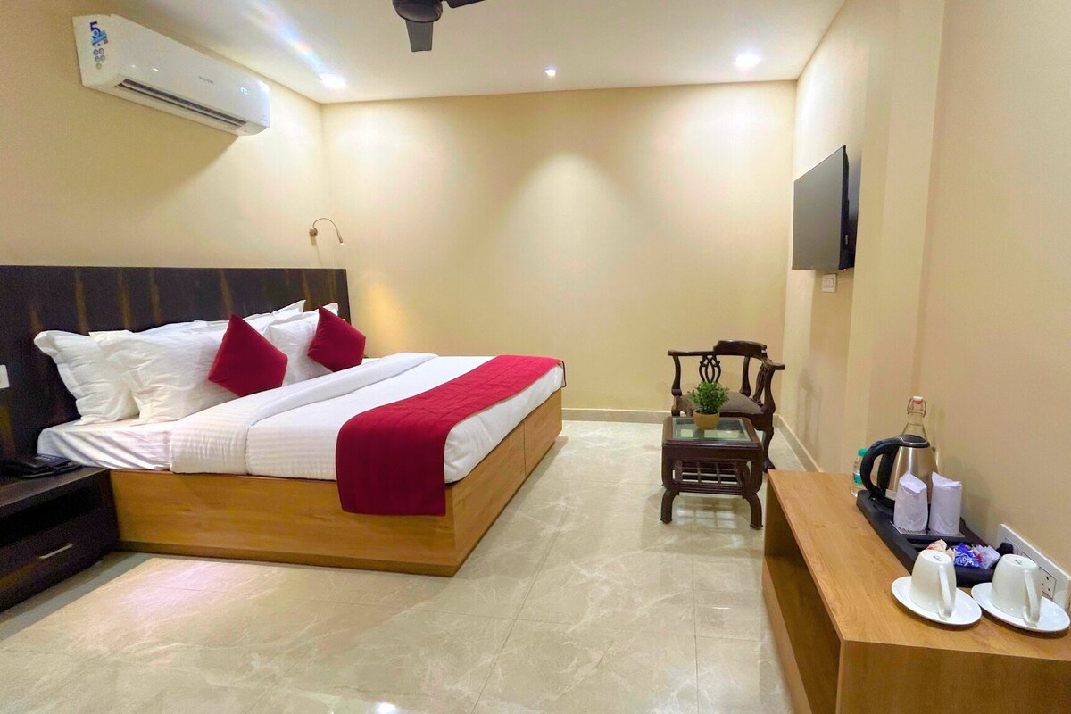 A hotel room with a bed, bedside table, TV, and a small table with a kettle and cups.