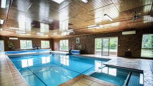 Une piscine intérieure dotée d’un plafond en bois, d’un sol carrelé et de grandes fenêtres.