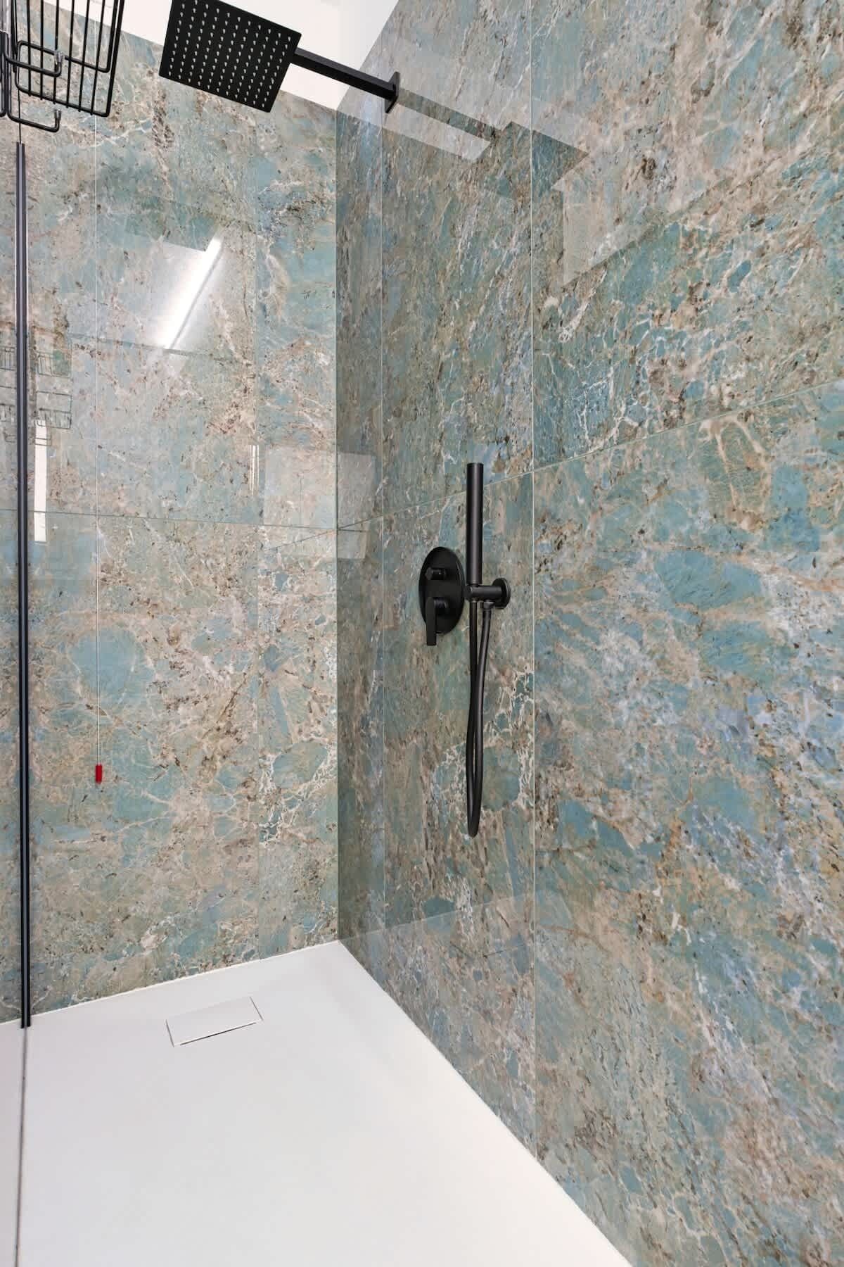 Une salle de bain moderne avec un mur en marbre, une pomme de douche noire et une paroi de douche en verre.