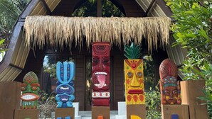 A wooden structure with a thatched roof and colorful totem poles labeled with letters. - Gila House (Gili Air)