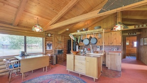 Ein rustikales Blockhaus-Interieur mit einem Holzespeisesaal, einer Küchenzeile mit hängenden Töpfen und einem großen Teppich.
