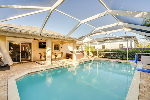 En swimmingpool med et overdækket terrasseområde, udendørs møbler og frit udsyn til himlen.