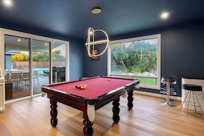 A pool table in a room with large windows, a bar area, and a view of the outdoors.