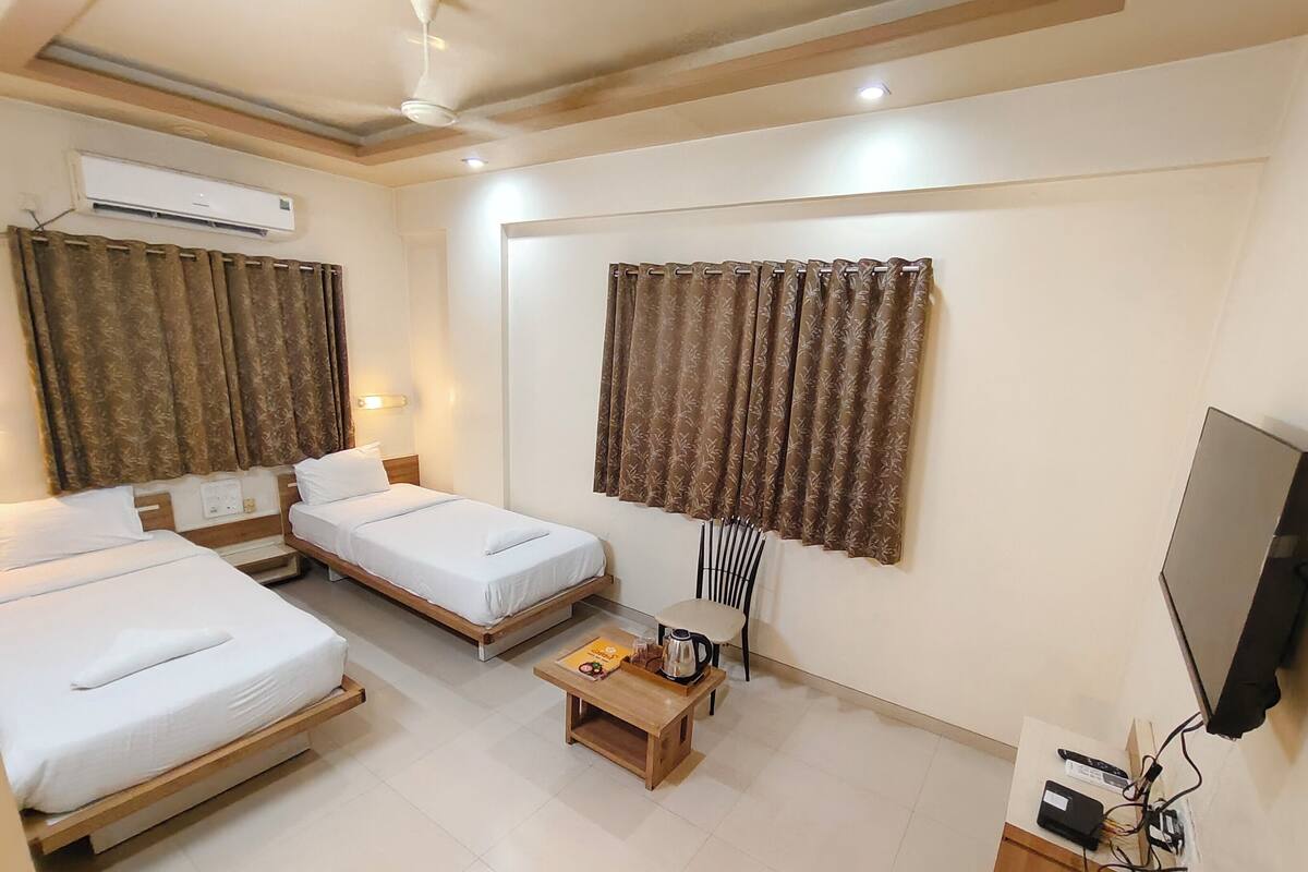 A hotel room with two single beds, a wooden coffee table, a chair, an air conditioner, and a TV.