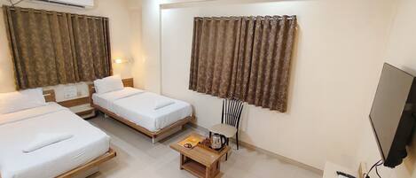 A hotel room with two single beds, a wooden coffee table, a chair, an air conditioner, and a TV.