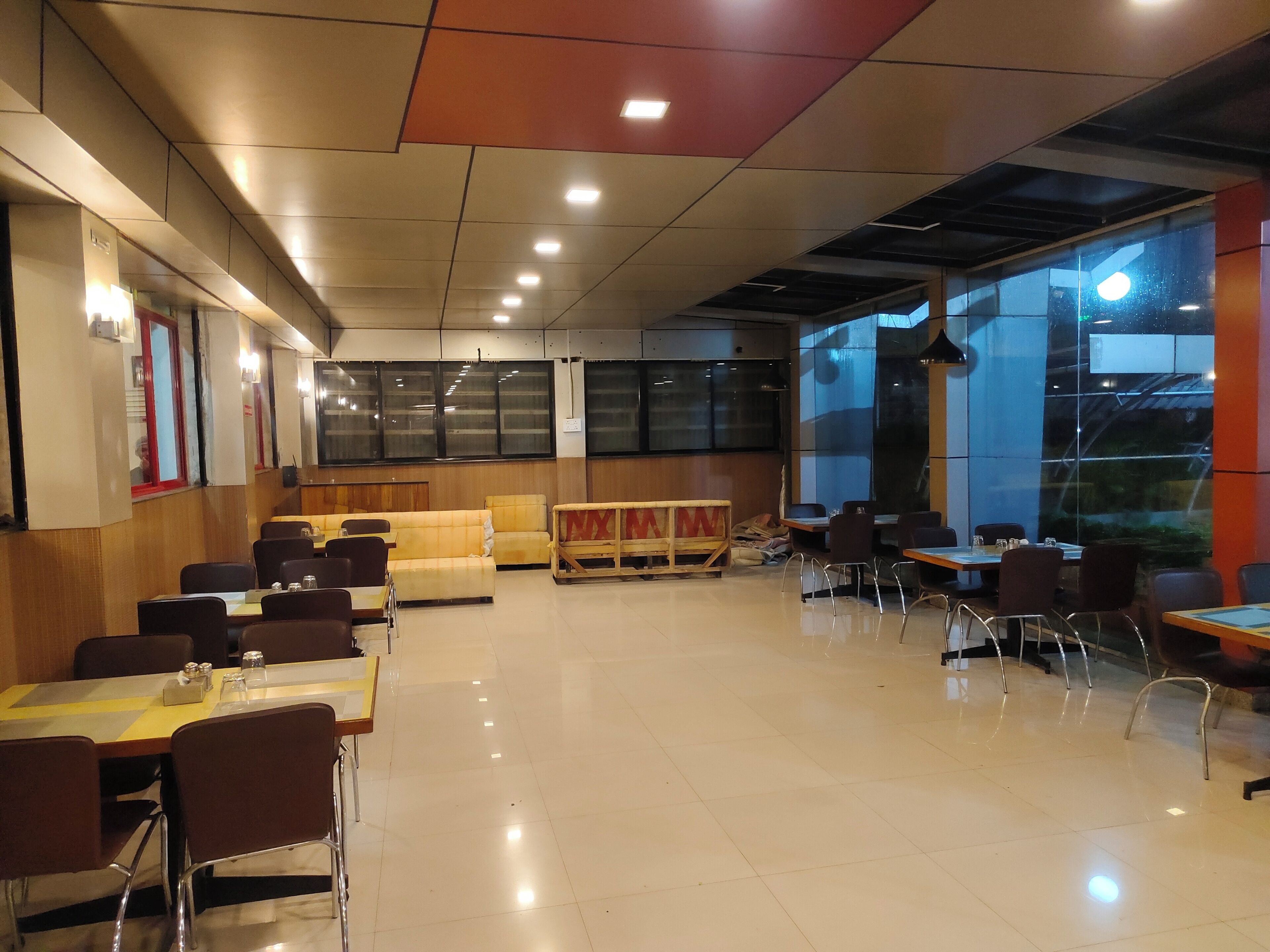 Un restaurante espacioso con techos altos, ventanas amplias y una variedad de asientos, incluyendo mesas y sofás.