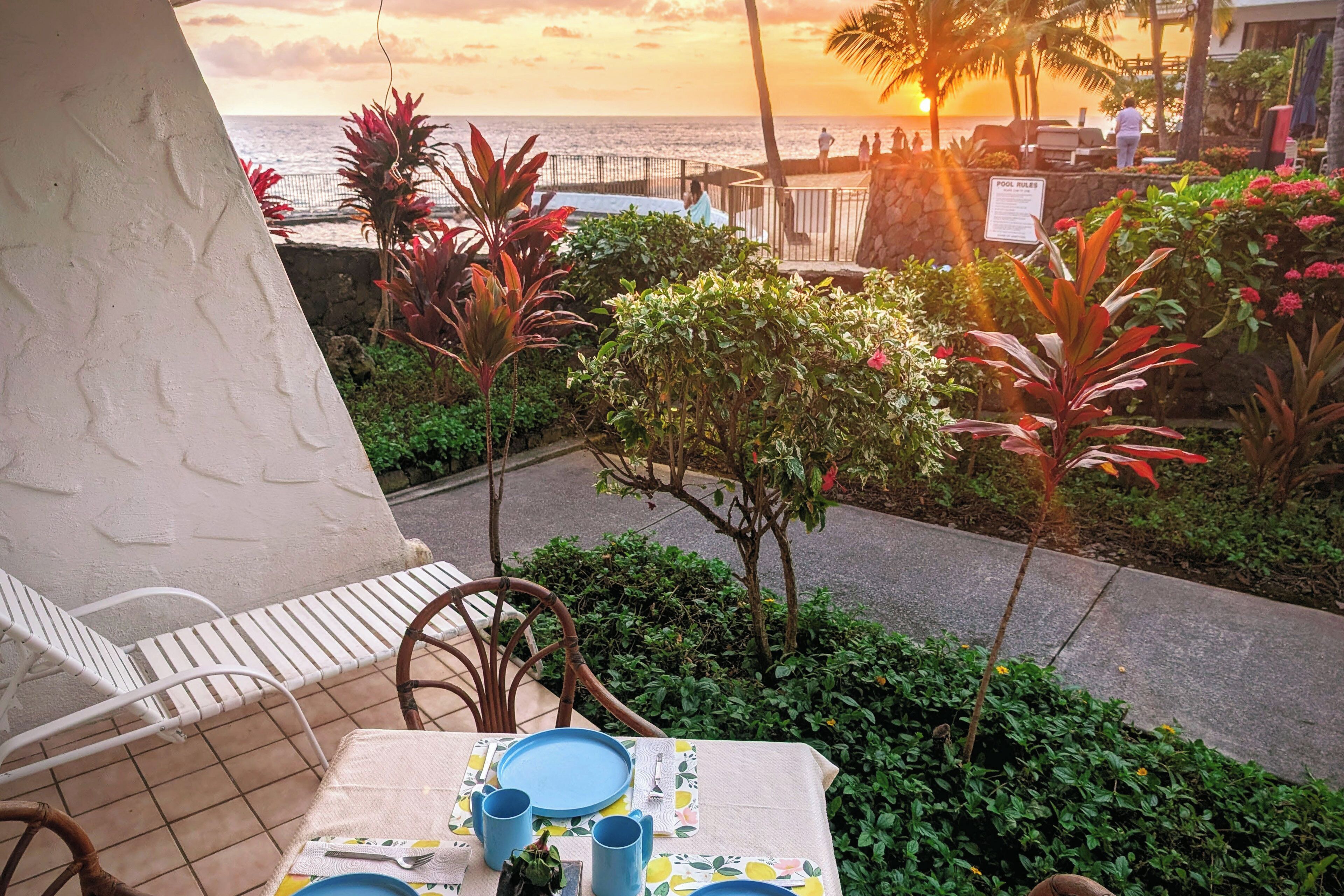 Terraço com mesa posta para refeição, vista para a praia e para o pôr do sol.