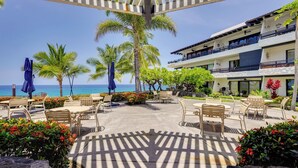 Eine Resort-Terrasse mit Sitzgelegenheiten im Freien, Palmen und Blick aufs Meer.