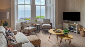 A living room with a large window overlooking the sea, a television, and a cozy seating area. - 3 bedroom accommodation in Blairmore, near Dunoon (Blairmore, near Dunoon)