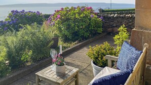 A patio with a wooden table and chairs, a bottle of champagne, and a view of the sea. - 3 bedroom accommodation in Blairmore, near Dunoon (Blairmore, near Dunoon)
