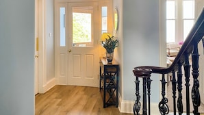 A hallway with a wooden floor, a white door, a small table with a plant, and a staircase with ornate black railings. - 3 bedroom accommodation in Blairmore, near Dunoon (Blairmore, near Dunoon)