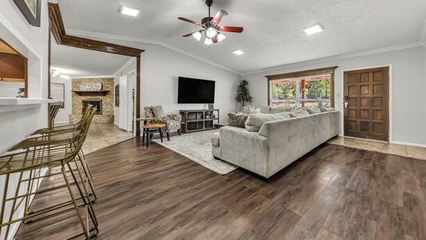 A spacious living room with a large sofa, a dining area with a wooden table and chairs, a ceiling fan, and a fireplace.