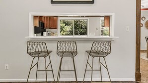 A kitchen with a window, three wireframe bar stools, and a framed picture above the window.