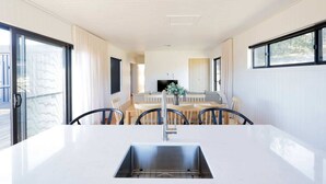 Eine moderne Küche mit einer zentralen Kochinsel, einem Essbereich mit Tisch und Stühlen sowie einem großen Fenster, das für natürliches Licht sorgt.