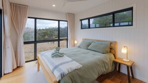 Ein Schlafzimmer mit Bett, Nachttischlampen, einem Fenster mit Blick auf Bäume und einem Deckenventilator.