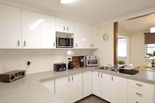 A modern kitchen with white cabinets, a microwave, a toaster, and a sink.