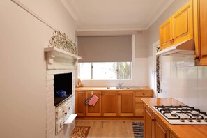 A kitchen with white brick walls, wooden cabinets, a gas stove, and a window with a view.