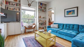 Una sala de estar con un sofá azul, una mesa de centro, una estantería, un televisor y un cuadro en la pared.