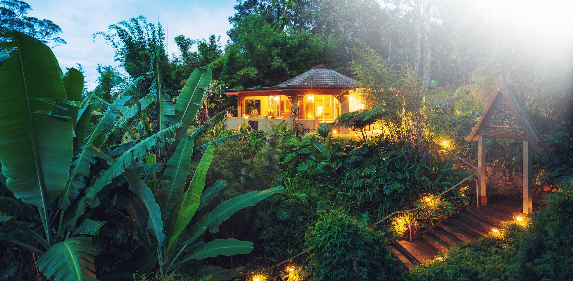 A secluded bungalow nestled in a lush, tropical garden with a small shrine-like structure nearby.