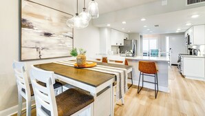 A modern kitchen with white cabinets, a wooden island, and a dining area with white chairs and a wooden table. - < 1 Mi to Fort Myers Beach: Bayfront Condo w/ Pool (Fort Myers Beach)