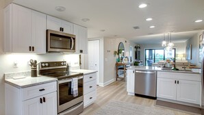 A modern kitchen with white cabinetry, stainless steel appliances, and a large island with a sink. - < 1 Mi to Fort Myers Beach: Bayfront Condo w/ Pool (Fort Myers Beach)