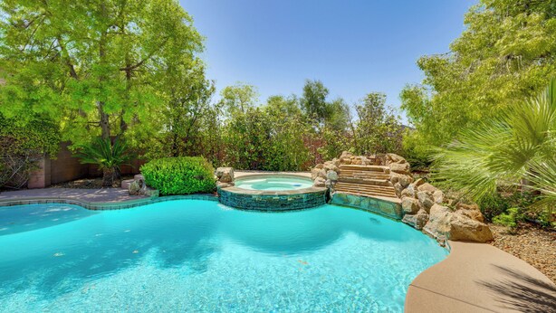 Piscina com hidromassagem, cercada por vegetação exuberante e um muro de pedra.