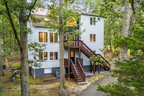 A two-story cabin with a wooden staircase and a deck, surrounded by trees.