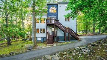 A two-story building with a wooden staircase leading to a balcony, surrounded by trees and a paved path.