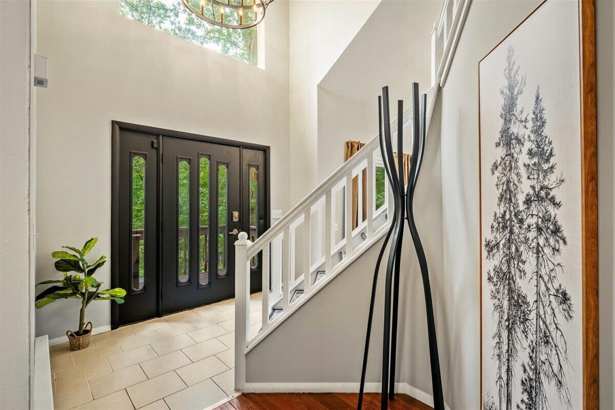 A staircase with a white railing, a black door with glass panels, and a framed black and white tree painting on the wall.
