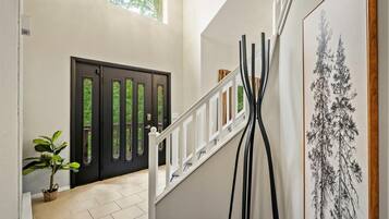 A staircase with a white railing, a black door with glass panels, and a framed black and white tree painting on the wall.