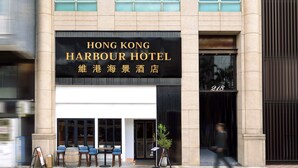 The exterior of the Hong Kong Harbour Hotel with a signboard, a seating area with chairs, and a person walking by. - Hong Kong Harbour Hotel (Hong Kong Island)