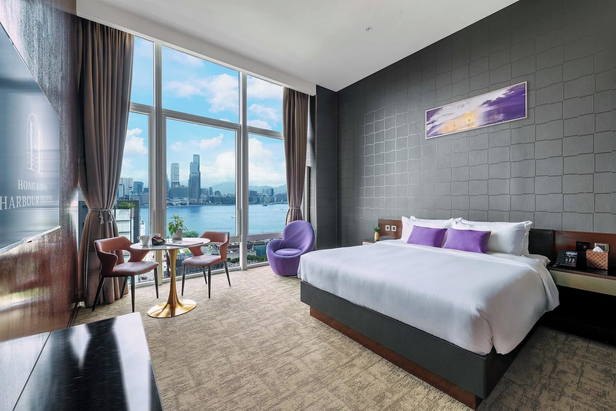 Quarto de hotel com uma cama grande, uma mesa, uma cadeira e vista para a cidade.
