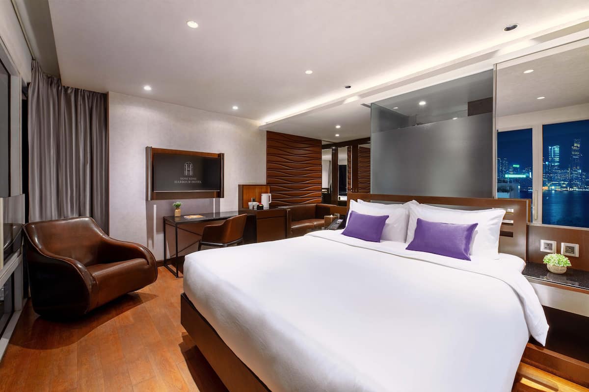 Quarto de hotel moderno com uma cama grande, uma escrivaninha, uma cadeira e vista para a cidade.