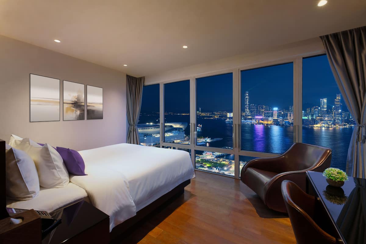 Quarto de hotel com uma cama grande, área de estar e vista noturna para a cidade e o mar.