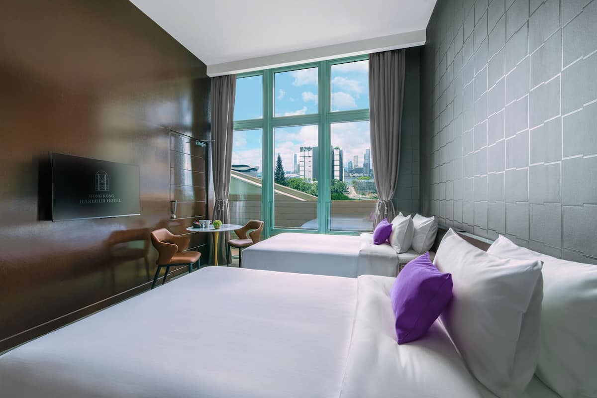 Quarto de hotel com uma cama grande, uma cama menor, uma escrivaninha e vista para a cidade.