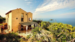 A two-story house with a balcony, a covered patio, and a view of the sea.