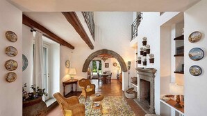 A spacious hallway with a high ceiling, a fireplace, wicker furniture, and decorative plates on the walls.