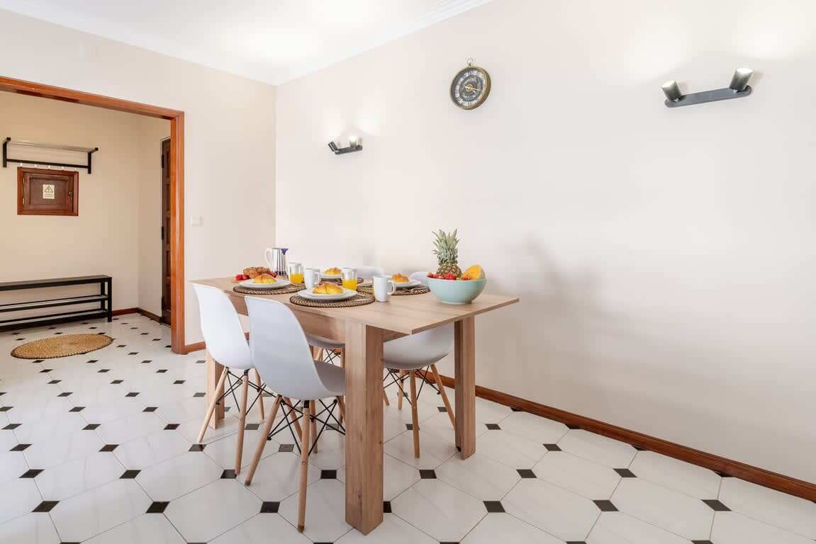 A dining area with a wooden table, white chairs, and a bowl of fruit.