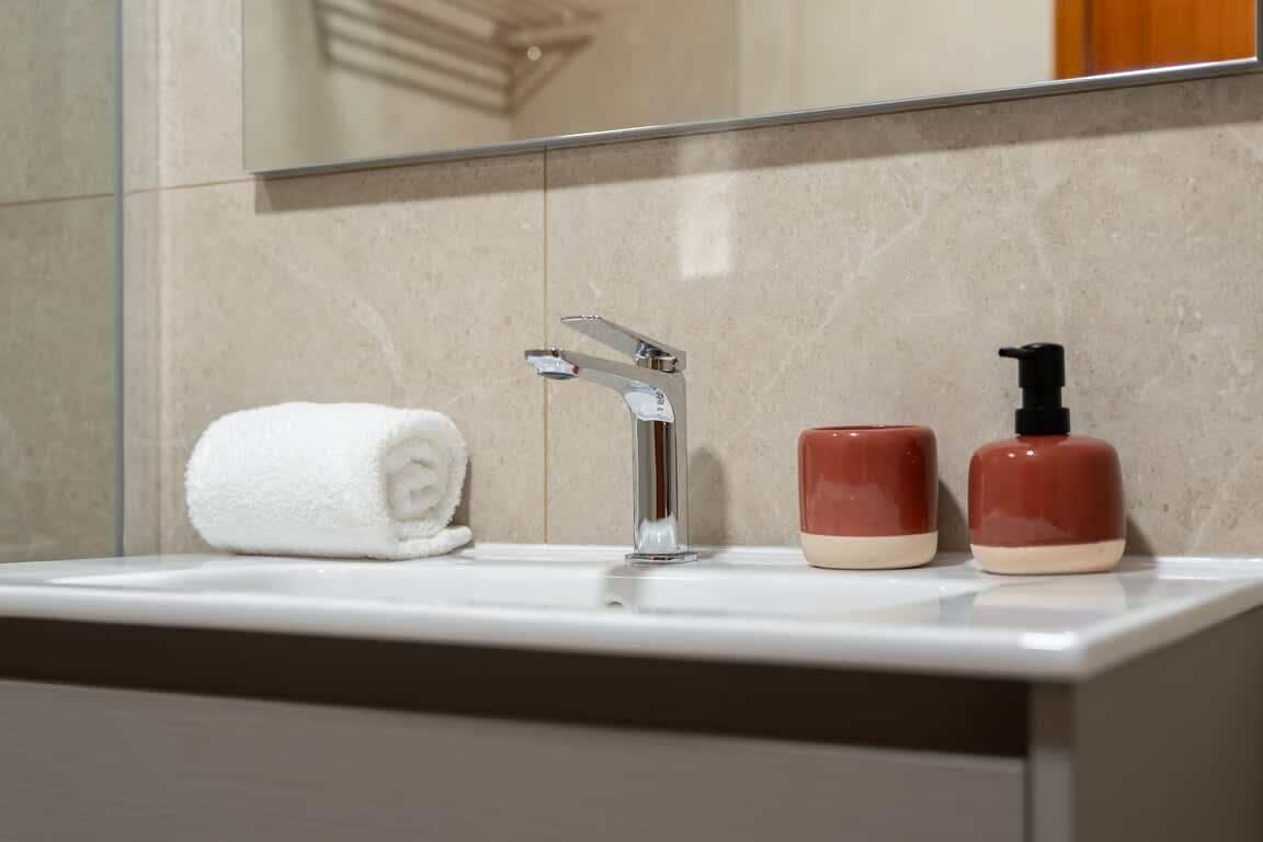 Un lavabo con una toalla, un grifo y dos dispensadores de jabón.