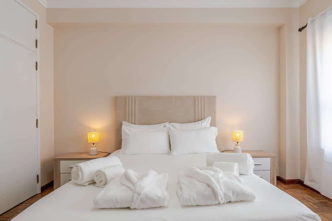 Una habitación de hotel con cama, dos lámparas de noche, una mesita de noche y un juego de toallas.