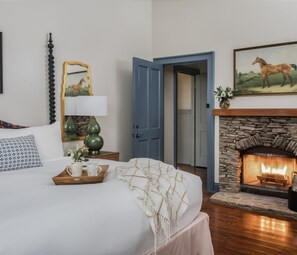 A bedroom with a bed, a nightstand with a lamp, a dresser, a blue door, a fireplace, and a painting of a horse. - Perfect Stay with Outdoor Adventures, Spa, and Outdoor Pool! (Adairsville)