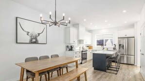 A modern kitchen with white cabinets, a stainless steel refrigerator, and a dining area with a wooden table and benches.