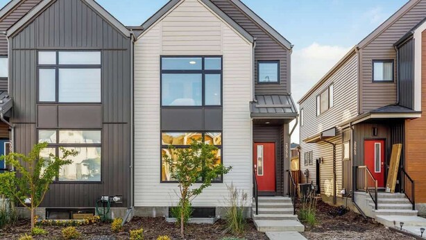A modern residential building with a central entrance, large windows, and a small front yard.