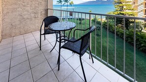 A balcony with a table and chairs, overlooking a beach and ocean. - Royal Kahana 404 (Lahaina)