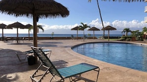 A poolside area with lounge chairs, umbrellas, and a view of the ocean. - Royal Kahana 404 (Lahaina)