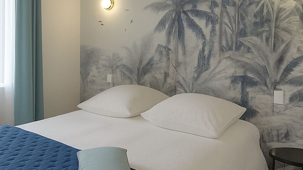 Ein Schlafzimmer mit einem Bett, einer blauen Tagesdecke und einer Wandmalerei von Palmen.