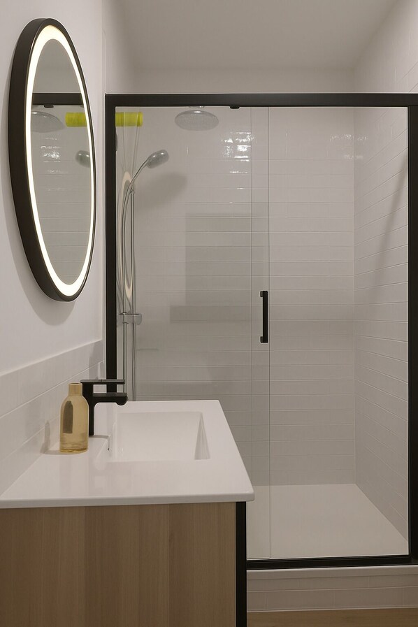 A modern bathroom with a white sink, a mirror, and a glass shower enclosure.