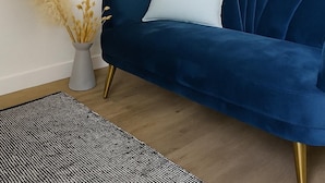 Ein modernes Wohnzimmer mit einem blauen Sofa, einer goldenen Stehlampe und einem gerahmten Bild an der Wand.