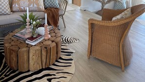 Een woonkamer met een bank, twee rieten fauteuils, een salontafel en een zebra vloerkleed, plus een schuifdeur in boerderijstijl.